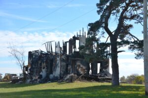Casa destruída com restos carbonizados e uma árvore
